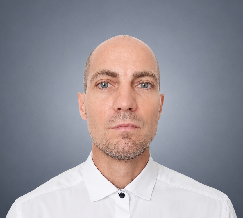 Professional portrait of Grégory Mastorgio wearing a white shirt against a blue-grey background.